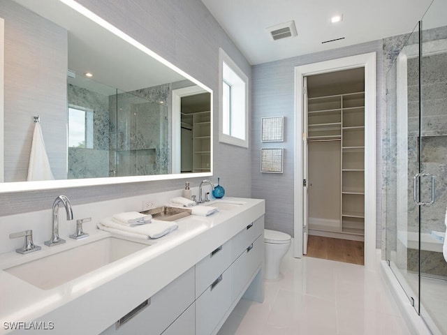 bathroom with a shower with shower door, tile walls, tile patterned flooring, vanity, and toilet