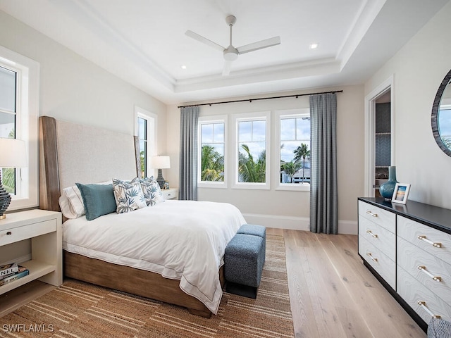 bedroom with ceiling fan, a tray ceiling, and light wood-type flooring