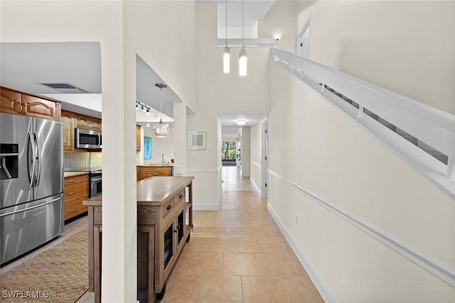 kitchen featuring light tile patterned floors, appliances with stainless steel finishes, hanging light fixtures, backsplash, and a towering ceiling