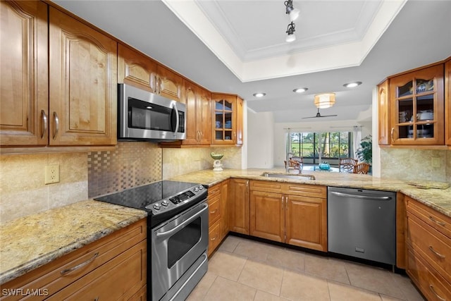 kitchen with light stone countertops, stainless steel appliances, a sink, brown cabinets, and a raised ceiling