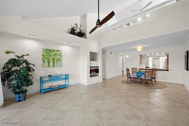 living room featuring light tile patterned floors, ceiling fan, a towering ceiling, a multi sided fireplace, and built in shelves