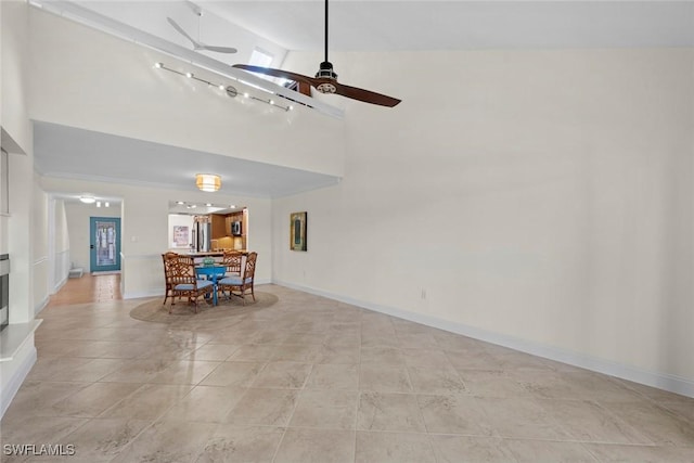 unfurnished living room with baseboards, a fireplace with raised hearth, ceiling fan, a high ceiling, and light tile patterned flooring