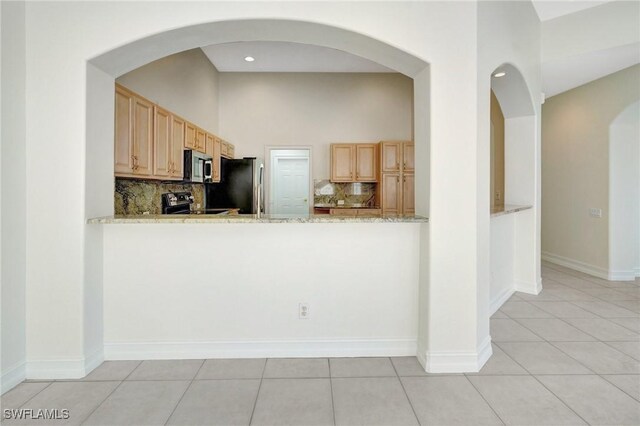 kitchen featuring light tile patterned flooring, appliances with stainless steel finishes, tasteful backsplash, light stone countertops, and light brown cabinets