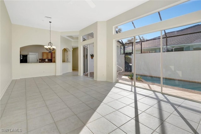 empty room with baseboards, light tile patterned flooring, arched walkways, and an inviting chandelier