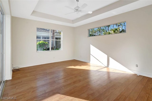 spare room featuring wood-type flooring, ceiling fan, baseboards, and a tray ceiling