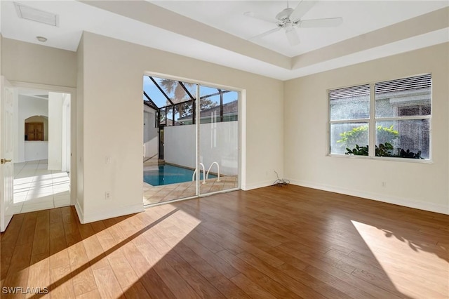 unfurnished room with a raised ceiling, plenty of natural light, dark hardwood / wood-style floors, and ceiling fan