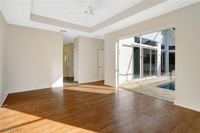 empty room with ceiling fan, baseboards, a tray ceiling, and wood-type flooring