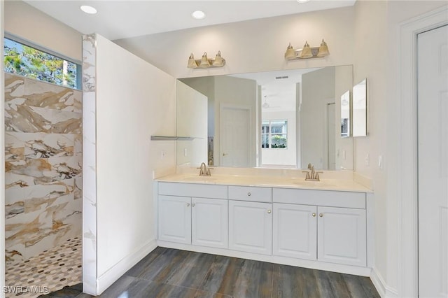 bathroom with wood finished floors, tiled shower, double vanity, a sink, and baseboards