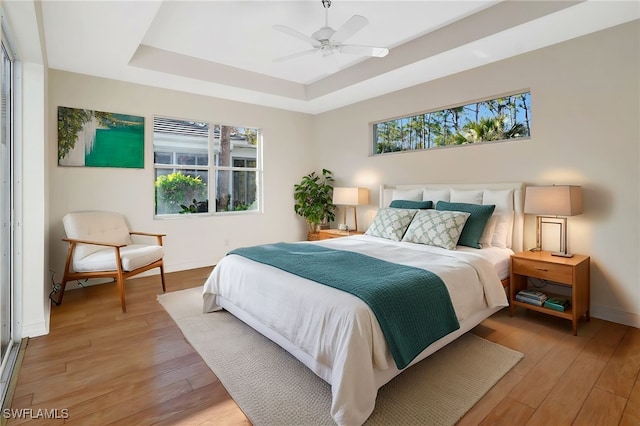 bedroom with ceiling fan, a tray ceiling, light wood-type flooring, and baseboards