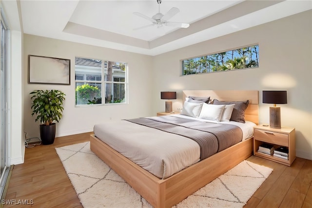 bedroom featuring baseboards, a raised ceiling, ceiling fan, and light wood-style floors