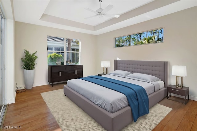 bedroom with a raised ceiling, a ceiling fan, light wood finished floors, and baseboards