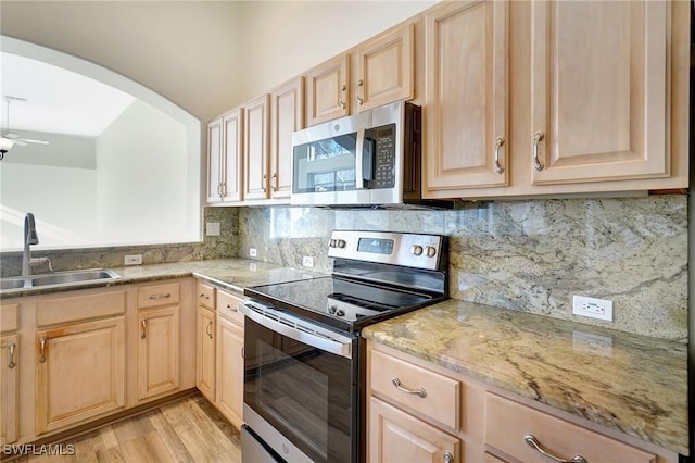 kitchen with light brown cabinetry, stainless steel appliances, arched walkways, and a sink