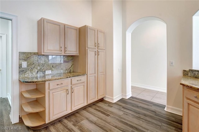kitchen with light stone countertops, open shelves, tasteful backsplash, arched walkways, and wood finished floors