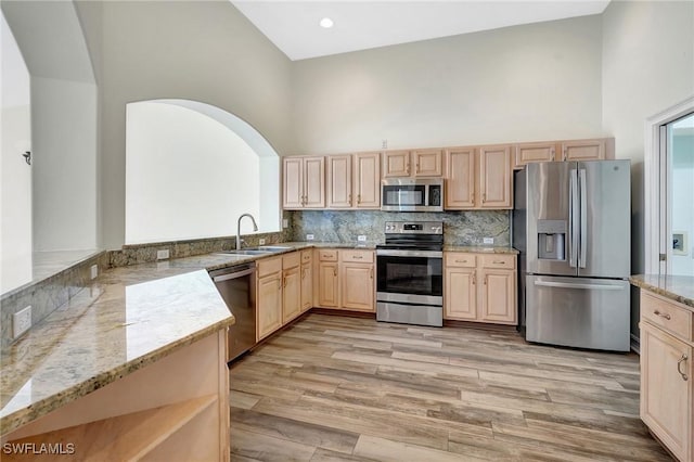 kitchen featuring light stone countertops, light brown cabinets, appliances with stainless steel finishes, a sink, and a towering ceiling