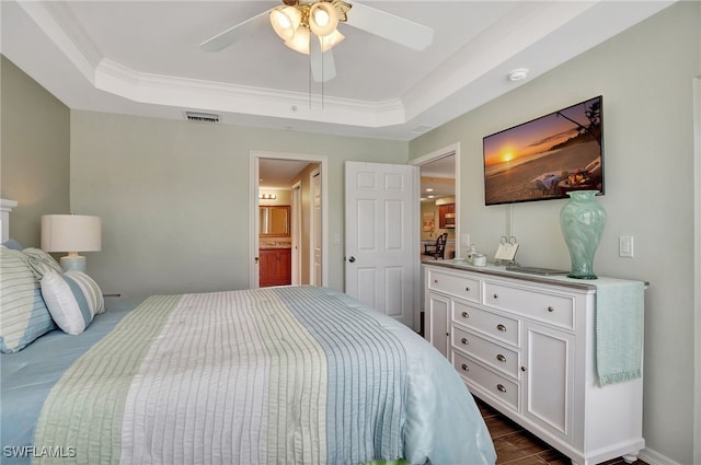 bedroom featuring dark wood-type flooring, ensuite bath, ornamental molding, a tray ceiling, and ceiling fan