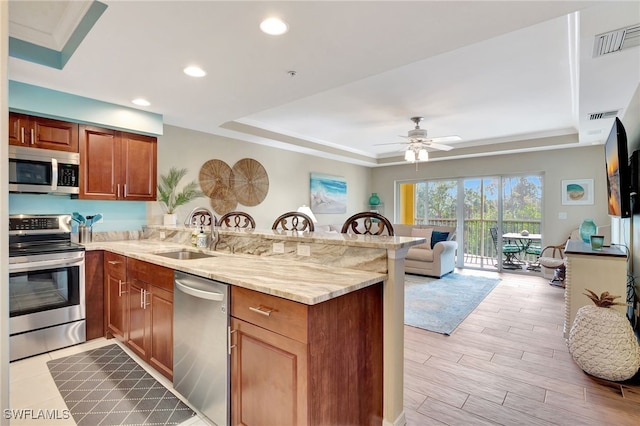 kitchen featuring stainless steel appliances, a tray ceiling, sink, and kitchen peninsula