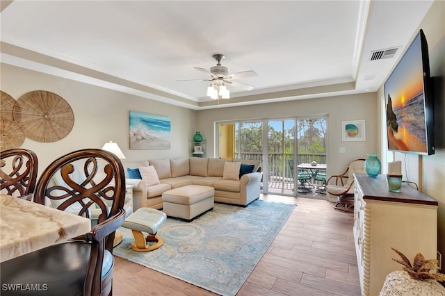 living room featuring crown molding, ceiling fan, wood-type flooring, and a tray ceiling