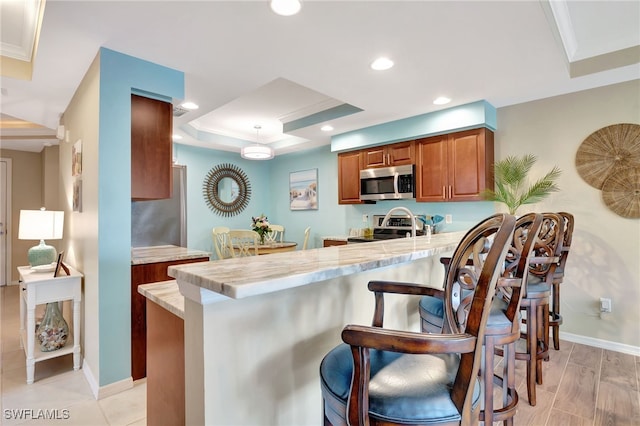 kitchen with a breakfast bar area, crown molding, a tray ceiling, kitchen peninsula, and stainless steel appliances