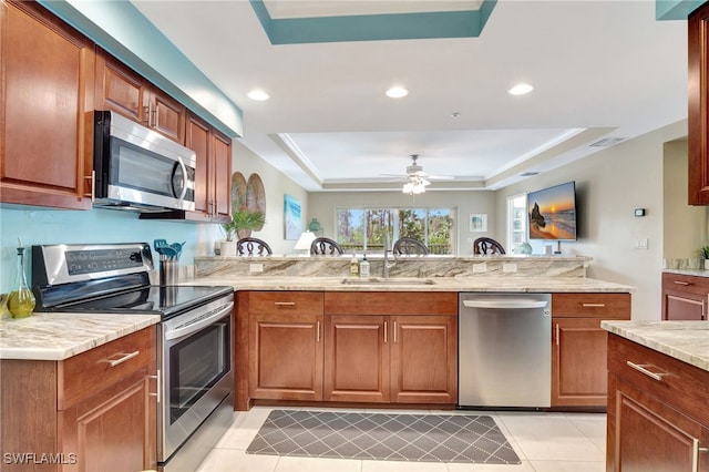 kitchen with stainless steel appliances, a raised ceiling, sink, and kitchen peninsula