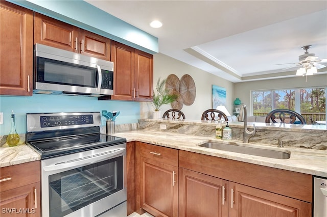 kitchen featuring light stone counters, ceiling fan, stainless steel appliances, and sink