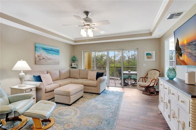 living room featuring hardwood / wood-style flooring, ornamental molding, a raised ceiling, and ceiling fan