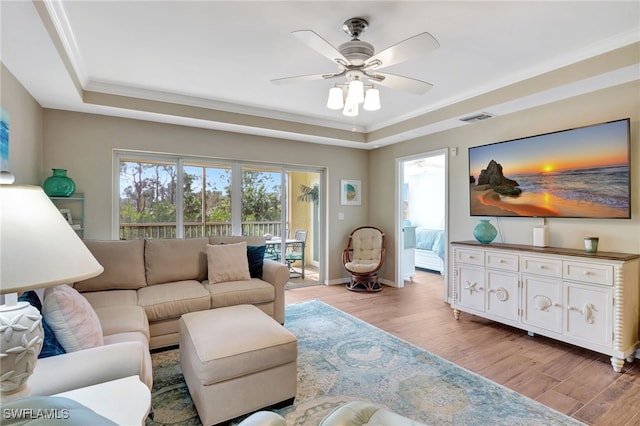 living room featuring a tray ceiling, crown molding, light hardwood / wood-style floors, and ceiling fan