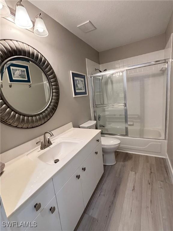 full bath featuring vanity, wood finished floors, shower / bath combination with glass door, a textured ceiling, and toilet