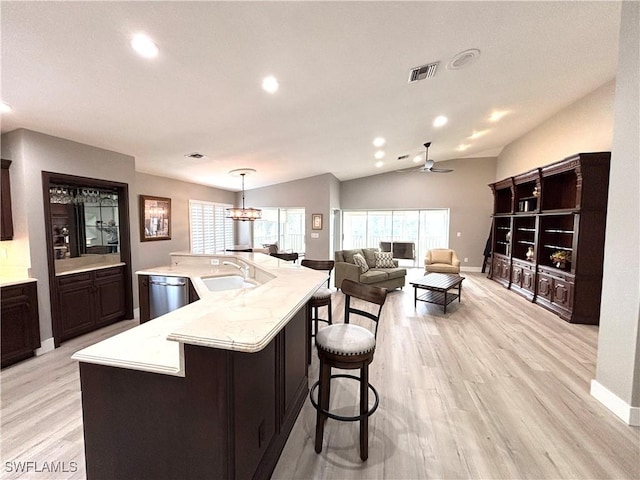 kitchen with pendant lighting, sink, dishwasher, a kitchen island with sink, and vaulted ceiling