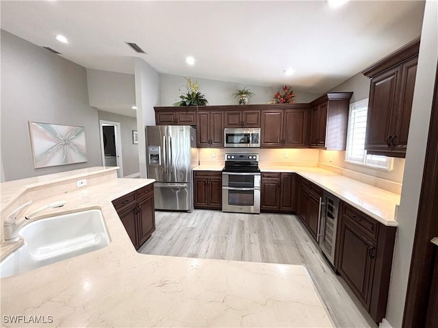 kitchen featuring visible vents, dark brown cabinets, vaulted ceiling, appliances with stainless steel finishes, and a sink