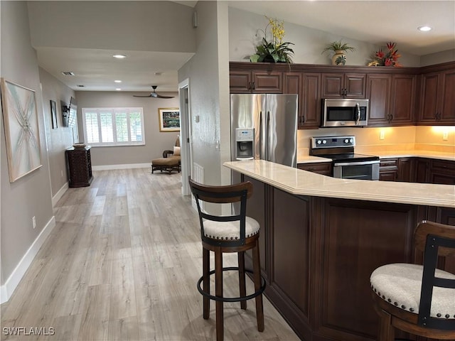 kitchen featuring a breakfast bar area, vaulted ceiling, dark brown cabinets, appliances with stainless steel finishes, and light hardwood / wood-style floors