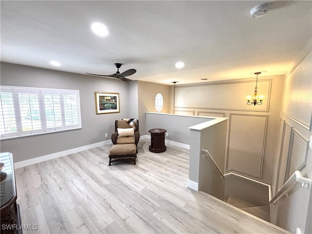 living area with ceiling fan with notable chandelier and light hardwood / wood-style flooring