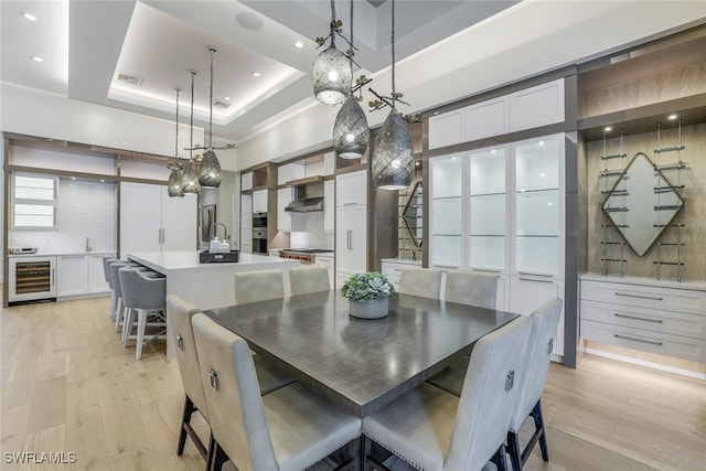 dining room with sink, a tray ceiling, beverage cooler, and light hardwood / wood-style floors