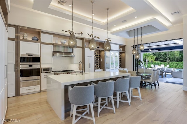 kitchen featuring white cabinetry, a tray ceiling, decorative light fixtures, and light hardwood / wood-style flooring