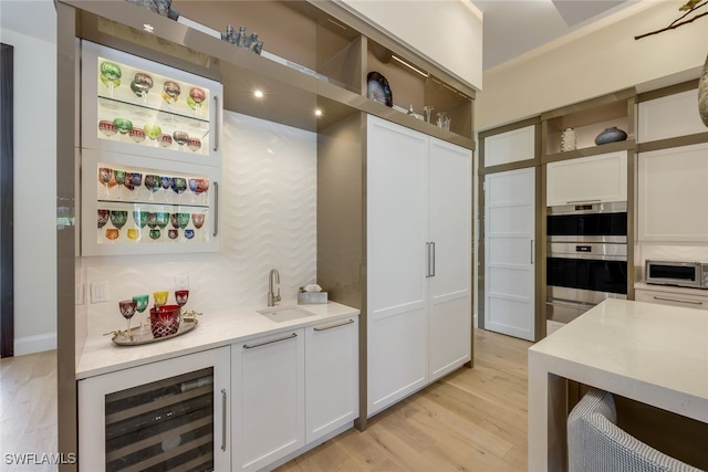 bar with sink, white cabinetry, decorative backsplash, beverage cooler, and light wood-type flooring