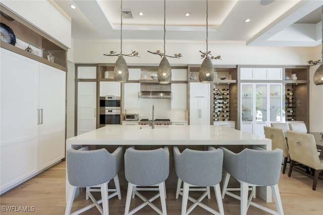 kitchen featuring a spacious island, hanging light fixtures, a tray ceiling, double oven, and white cabinets