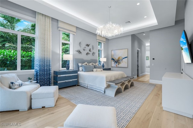 bedroom featuring an inviting chandelier, light hardwood / wood-style floors, and a raised ceiling