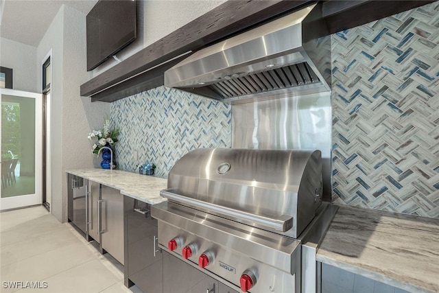 kitchen featuring backsplash, light tile patterned floors, light stone countertops, and wall chimney exhaust hood