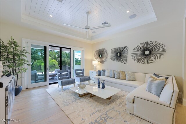 living room featuring a tray ceiling, light hardwood / wood-style flooring, ornamental molding, and ceiling fan