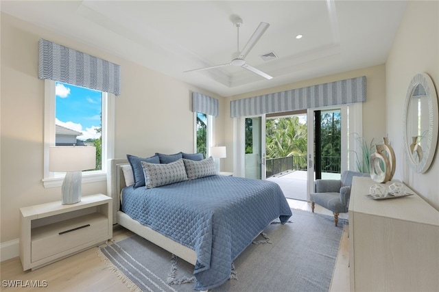 bedroom featuring ceiling fan, a tray ceiling, light hardwood / wood-style flooring, and access to outside