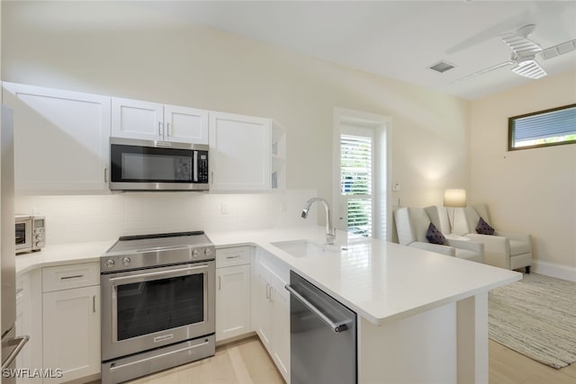 kitchen featuring stainless steel appliances, kitchen peninsula, sink, and white cabinets