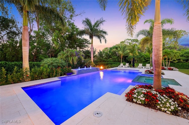 pool at dusk featuring an in ground hot tub and a patio