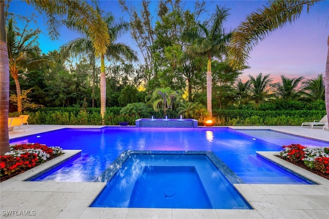 pool at dusk with an in ground hot tub, pool water feature, and a patio