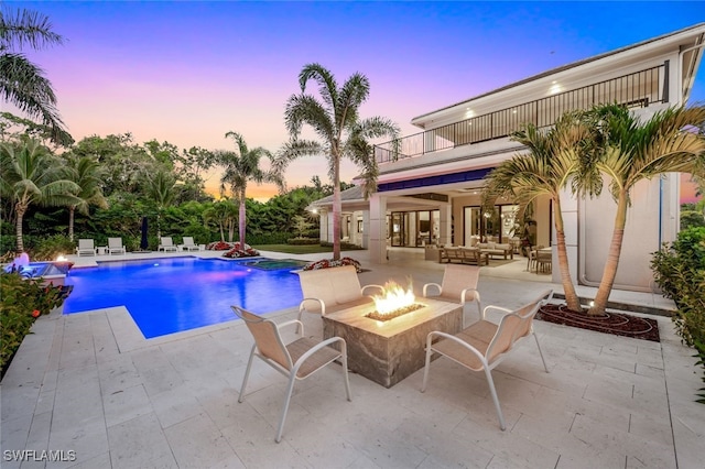 pool at dusk featuring a patio, pool water feature, and an outdoor living space with a fire pit