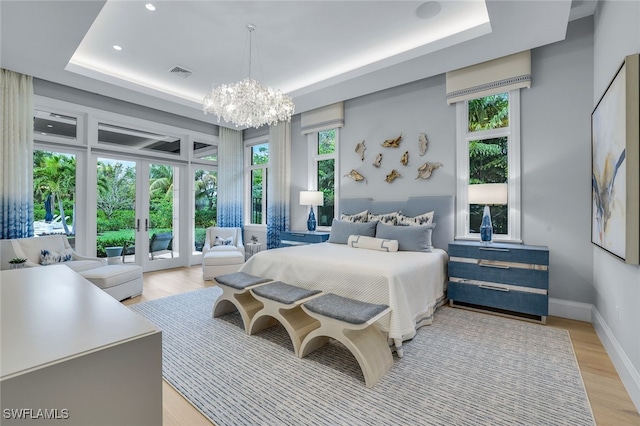 bedroom featuring an inviting chandelier, light hardwood / wood-style flooring, access to outside, a raised ceiling, and multiple windows