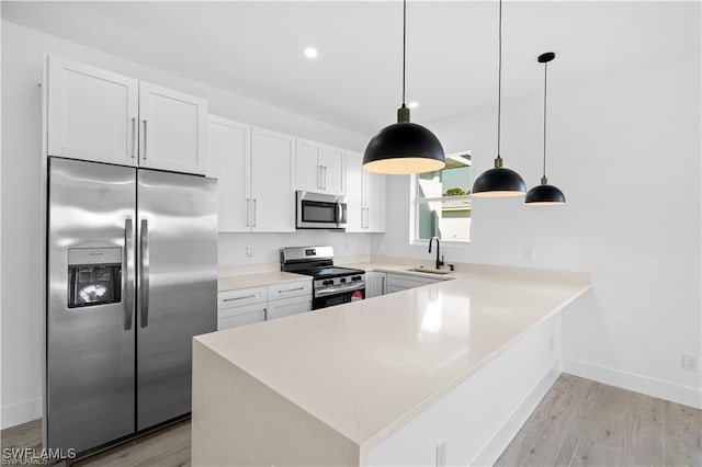 kitchen with decorative light fixtures, sink, white cabinets, stainless steel appliances, and light hardwood / wood-style flooring