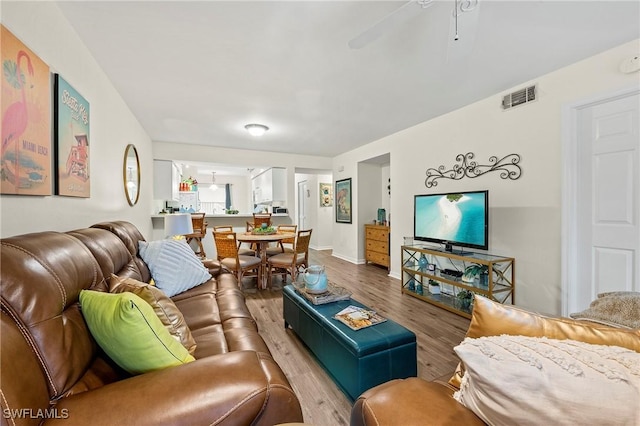 living area featuring baseboards, wood finished floors, visible vents, and a ceiling fan