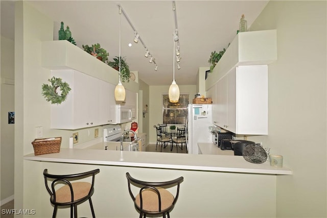 kitchen featuring white cabinetry, decorative light fixtures, white appliances, and kitchen peninsula