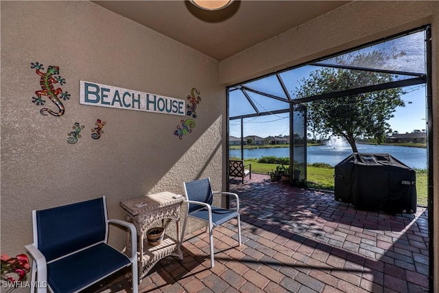 view of patio with area for grilling, glass enclosure, and a water view