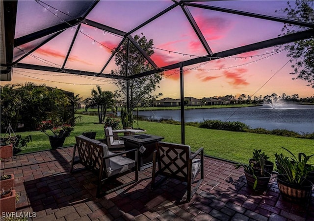 patio terrace at dusk featuring a water view, an outdoor fire pit, and a lawn