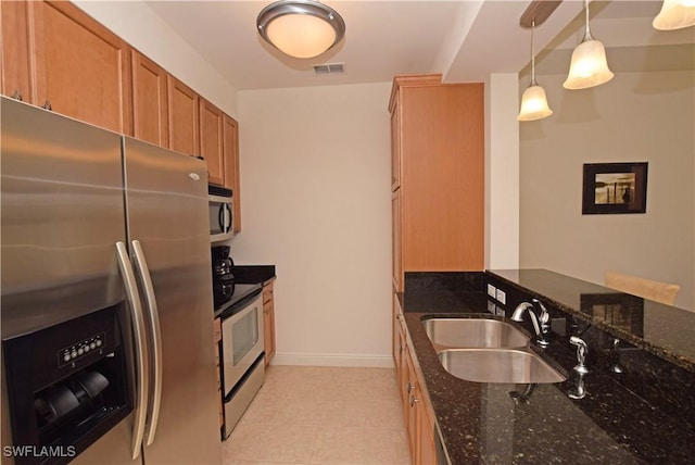 kitchen with hanging light fixtures, appliances with stainless steel finishes, sink, and dark stone countertops